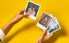 Hands holding and displaying several Polaroid photos against a bright yellow background. Voir les images du produit