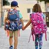 Two children walking hand-in-hand, wearing backpacks. Produktbild-Vorschau