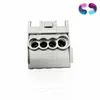 A close-up studio shot of a gray electrical connector with four openings, set against a white background. A colorful logo is visible in the upper right corner. Produktbild-Vorschau