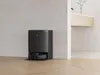 A black robot vacuum cleaner and its charging station are shown in a modern, minimalist room. Produktbild-Vorschau