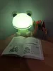 A frog-shaped LED night light illuminates a desk with an open book and a cup of pens. Náhľad obrázku produktu
