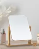 A wooden framed mirror sits on a table with some cosmetic products in the background. Produktbild-Vorschau
