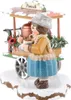 A wooden figurine of a girl selling punch from a cart in the snow. Produktbild-Vorschau