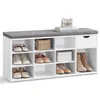 A white shoe bench with a gray upholstered top, featuring multiple compartments and a drawer, displaying various shoes and a decorative basket and box. Produktbild-Vorschau