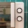 A close-up view of the control panel of a silver microwave oven, with green tiled wall in the background. Produktbild-Vorschau