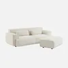A cream-colored bouclé upholstered ottoman is placed next to a cream-colored bouclé upholstered sofa. Produktbild-Vorschau