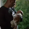 A man is holding a baby and a baby bottle. Produktbild-Vorschau