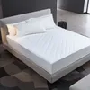 A white quilted mattress protector is shown on a bed with pillows. Náhled obrázku produktu