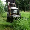 A person is using a rotary mower to cut tall grass in an outdoor setting with trees and vegetation. Produktbild-Vorschau