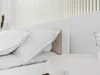 A close-up view of a white bed with white pillows and a light brown headboard. Náhled obrázku produktu