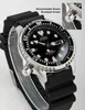 A close-up shot of a Citizen Promaster dive watch with a black dial and black rubber strap, displayed on a clear stand. Produktbild-Vorschau