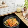 A close-up shot of a salmon fillet being cooked in a frying pan with vegetables on a stovetop. Produktbild-Vorschau