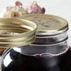 A close-up shot of a Kilner jar filled with a dark liquid, with its lid and screw band partially removed. Garlic bulbs are visible in the blurred background. Podgląd zdjęcia produktu