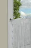 A close-up view of a white lace curtain hanging on a metal rod attached to a window frame, with a tree and sky visible outside. Produktbild-Vorschau