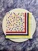 A white plate with a polka dot napkin on top, set against a blue textured background. Produktbild-Vorschau