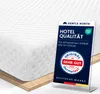 A close-up of a white mattress topper with a marketing display card in front of it. Produktbild-Vorschau