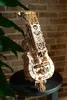 A wooden 3D puzzle of a musical instrument sits on a dark stool in front of a brick wall and a plant. Produktbild-Vorschau