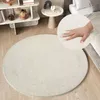 A round, cream-colored rug is shown in a bedroom setting, with a hand gently pressing into its soft surface. Náhľad obrázku produktu