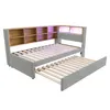 A light gray upholstered daybed with a built-in bookshelf headboard and a pull-out trundle bed, shown against a white background. Náhled obrázku produktu