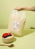 A hand holding a large bag of oats over a bowl of oatmeal with berries. Produktbild-Vorschau
