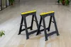 Two black and yellow sawhorses are placed on a light-colored wooden floor. Produktbild-Vorschau