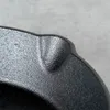 A close-up view of the textured surface and curved edge of a black cast iron pan. Produktbild-Vorschau