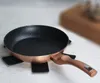 A frying pan is placed on a white surface with a wooden cutting board blurred in the background. Voir les images du produit