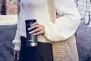 A person holding a travel mug while wearing a sweater and carrying a bag. Podgląd zdjęcia produktu