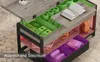 A coffee table with its top lifted to reveal storage compartments, some of which are highlighted with colored overlays. Produktbild-Vorschau