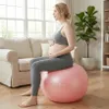 A pregnant woman is sitting on a pink exercise ball in a living room. Náhled obrázku produktu