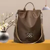 Braune Rucksack-Handtasche mit silbernem ineinandergreifendem Logo, einem oberen Griff und einem Schultergurt, neben einer Vase mit weißen Blumen Anteprima dell’immagine prodotto