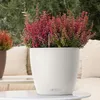 A white planter with pink flowers sits on a table outdoors, with a couch and greenery in the background. Náhľad obrázku produktu