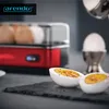 A red egg cooker with eggs inside, and two halves of a hard-boiled egg seasoned with pepper on a dark slate surface. Podgląd zdjęcia produktu