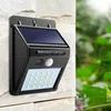 A solar-powered wall light with LEDs and a PIR sensor is mounted on a stone wall, with greenery and sunlight in the background. Produktbild-Vorschau