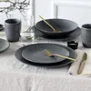 A table setting with dark gray stoneware plates, bowls, and cups, accented with gold cutlery and a glass of water. Náhľad obrázku produktu