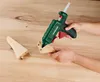A person is using a green hot glue gun to attach two pieces of wood together on a wooden surface. Produktbild-Vorschau