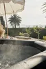 A steaming hot tub is shown in a garden setting with a palm tree and umbrella. Produktbild-Vorschau