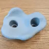 A light blue climbing hold with two holes is placed on a wooden surface. Voir les images du produit