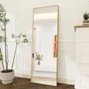 A full-length mirror with a gold frame stands in a room next to a potted plant and a white dresser. Náhled obrázku produktu