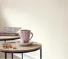 A still life arrangement on two round tables, featuring books, a pink mug with a small treat, and jewelry. Produktbild-Vorschau
