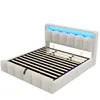 A beige upholstered bed frame with a slatted mattress base and blue LED lighting in the headboard, shown against a white background. Náhled obrázku produktu