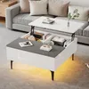 A modern living room scene featuring a multifunctional coffee table with its top lifted, revealing storage compartments. The table is placed in front of a sofa, with decorative items and books on display. Produktbild-Vorschau