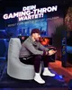 A man is playing video games while sitting on a large gray beanbag chair in a dimly lit room. Produktbild-Vorschau