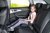 A young girl sits in the back seat of a car, looking at the camera. The sun is setting outside the car window. Produktbild-Vorschau