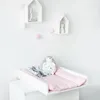 A baby changing station with a stuffed hedgehog and folded baby clothes. Produktbild-Vorschau