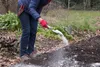 A person is applying white powder to the soil in a garden. Produktbild-Vorschau