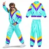 A man wearing an 80s/90s style tracksuit, posing with one hand raised. The tracksuit is displayed on the left, and a separate set of the tracksuit (jacket and pants) is shown on the right. Anteprima dell’immagine prodotto