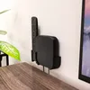 A black wall mount holder for a TV box and remote control is attached to a white wall above a wooden table. Produktbild-Vorschau