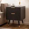 A modern black nightstand with gold accents is placed next to a sofa in a bedroom setting. Produktbild-Vorschau