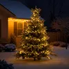 A decorated Christmas tree in the snow outside a house at night. Produktbild-Vorschau